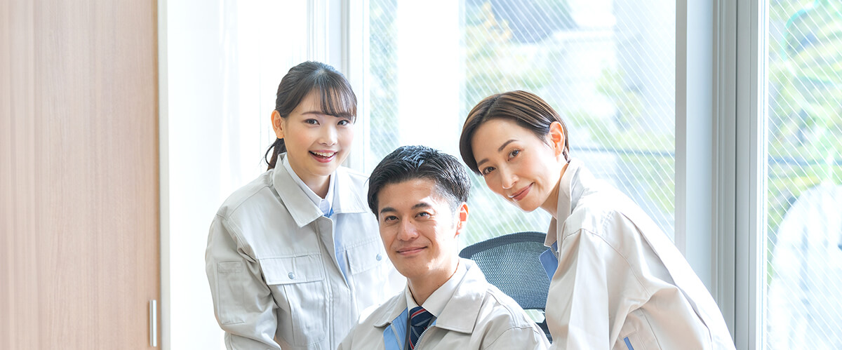 明るいオフィスで笑顔を見せる3人のスタッフ。制服を着用し、協力的な雰囲気が伝わる。